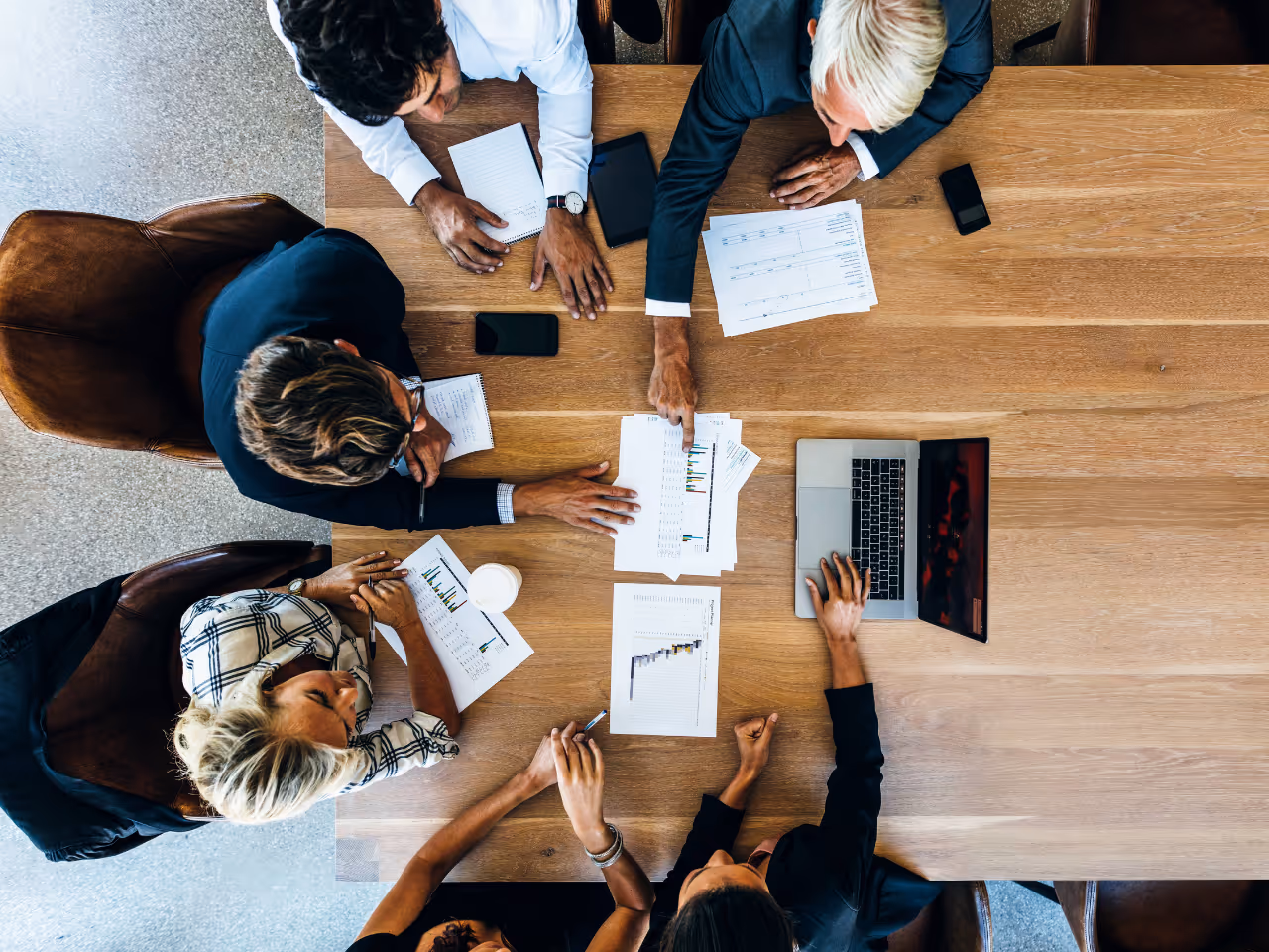 An overhead view of workers gathered around a table pointing at charts and graphs laid out.