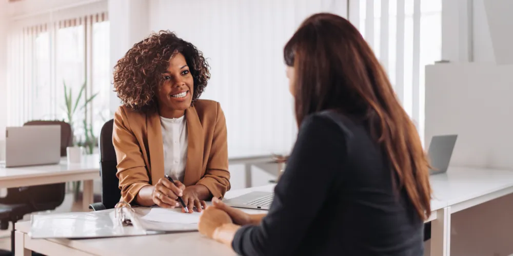 A woman sitting at a desk talking to another woman.