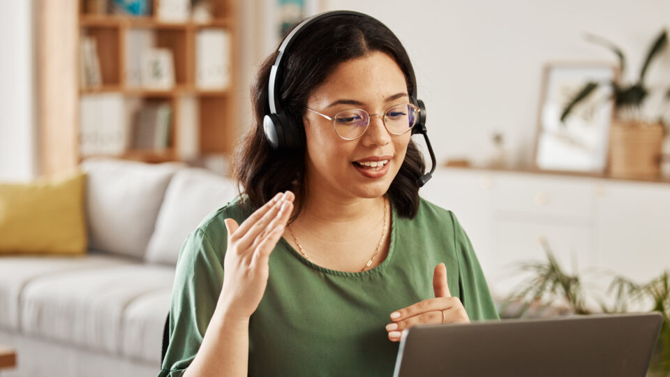 A woman wearing a phone headset is explaining something using her hands with a computer screen in front of her.