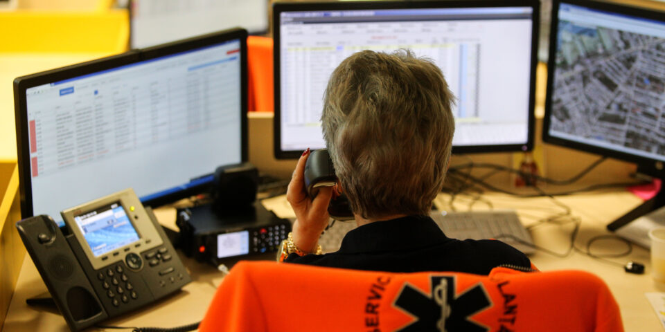An emergency dispatcher talks on the phone while looking at a series of computer monitors.