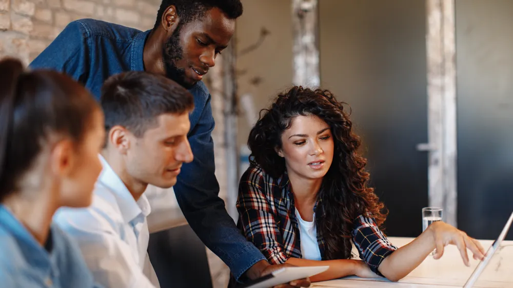 Diverse coworkers look at shared tablet screen.
