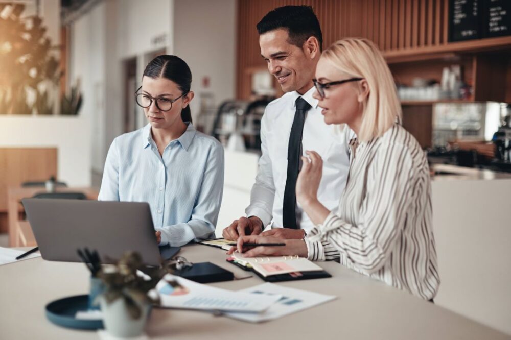 Three people sitting at a table looking at a laptop.