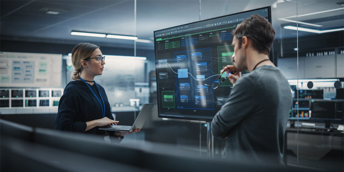 A man and a woman standing in front of a computer screen.