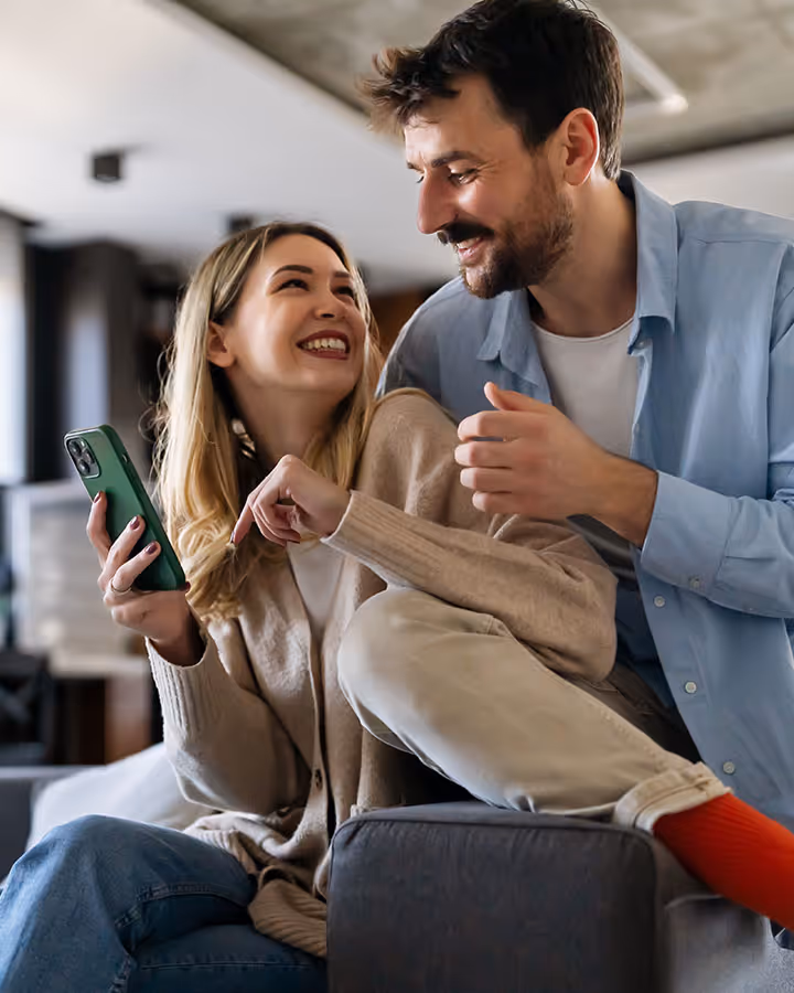 Image of a couple seated and smiling at each other and looking at phone