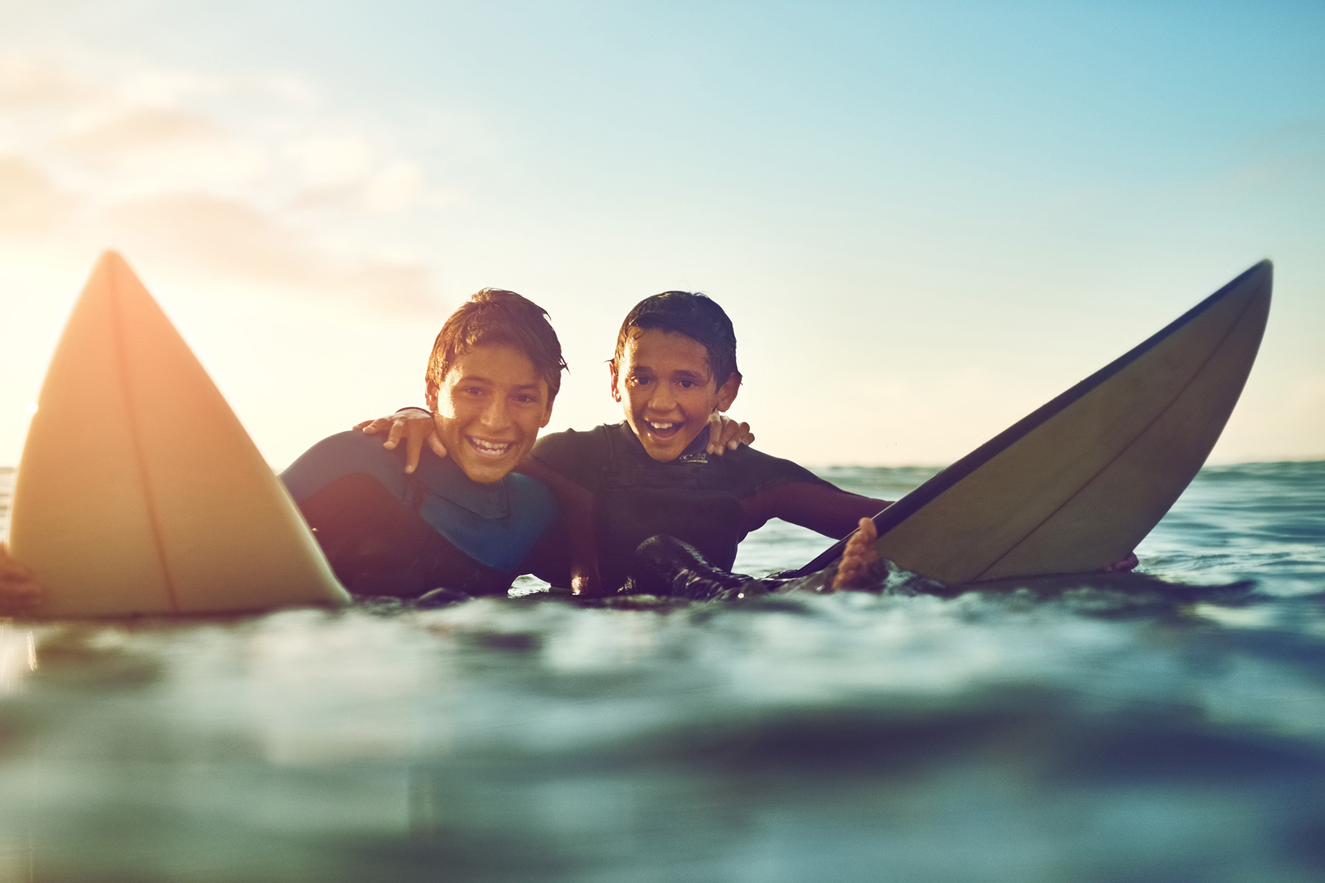 Two smiling young surfers in the water at sunset