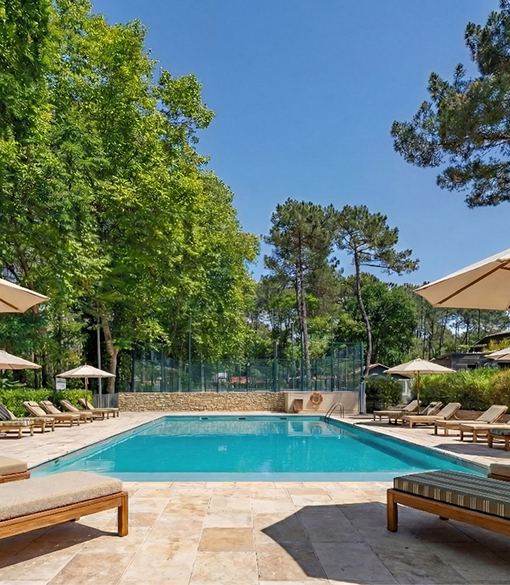 Zwembad omgeven door ligstoelen en parasols, groene bomen rondom