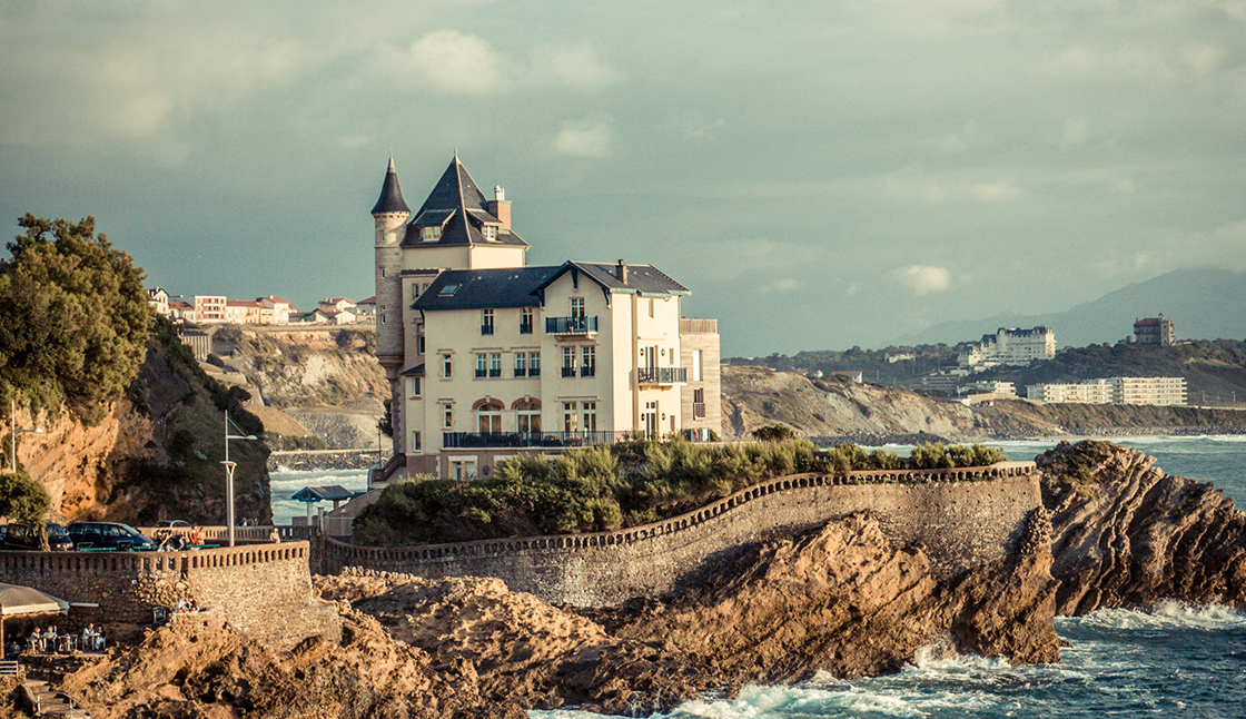 View of an ancient building with turrets on a rocky cliff bordered by the ocean