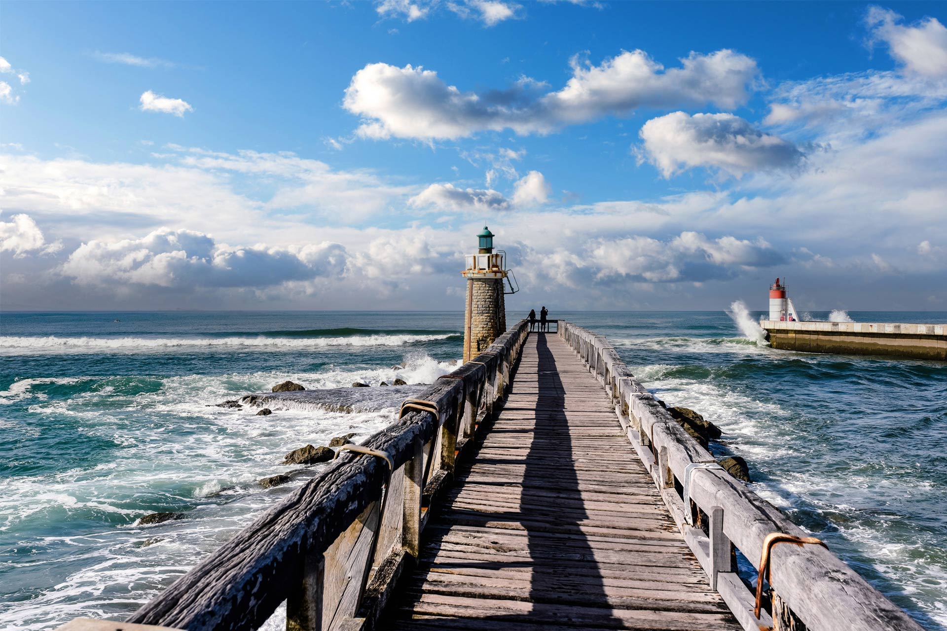 Wooden pontoon leading to a stone lighthouse by the ocean 