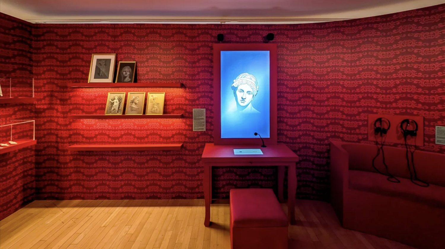 An Ask Mona avatar of the Venus of Arles on a screen in a red exhibition room
