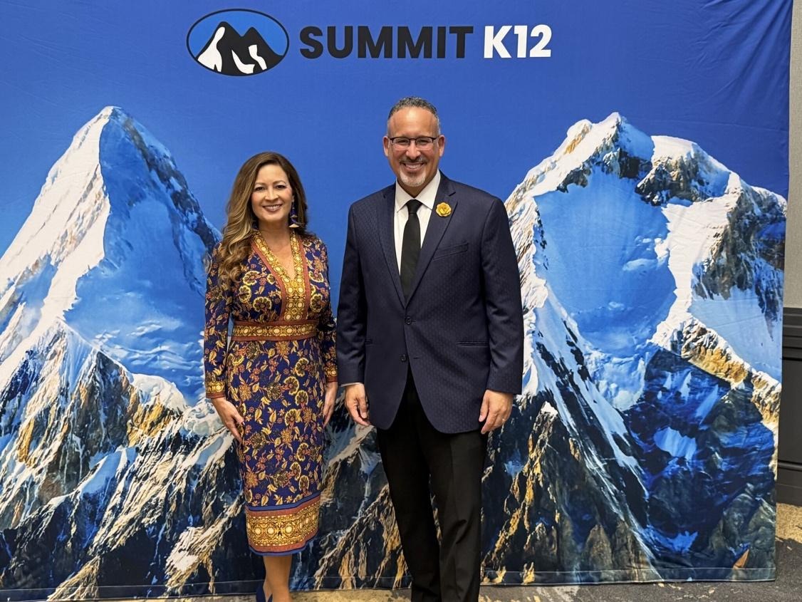 A person and person standing in front of a mountain backdropAI-generated content may be incorrect.