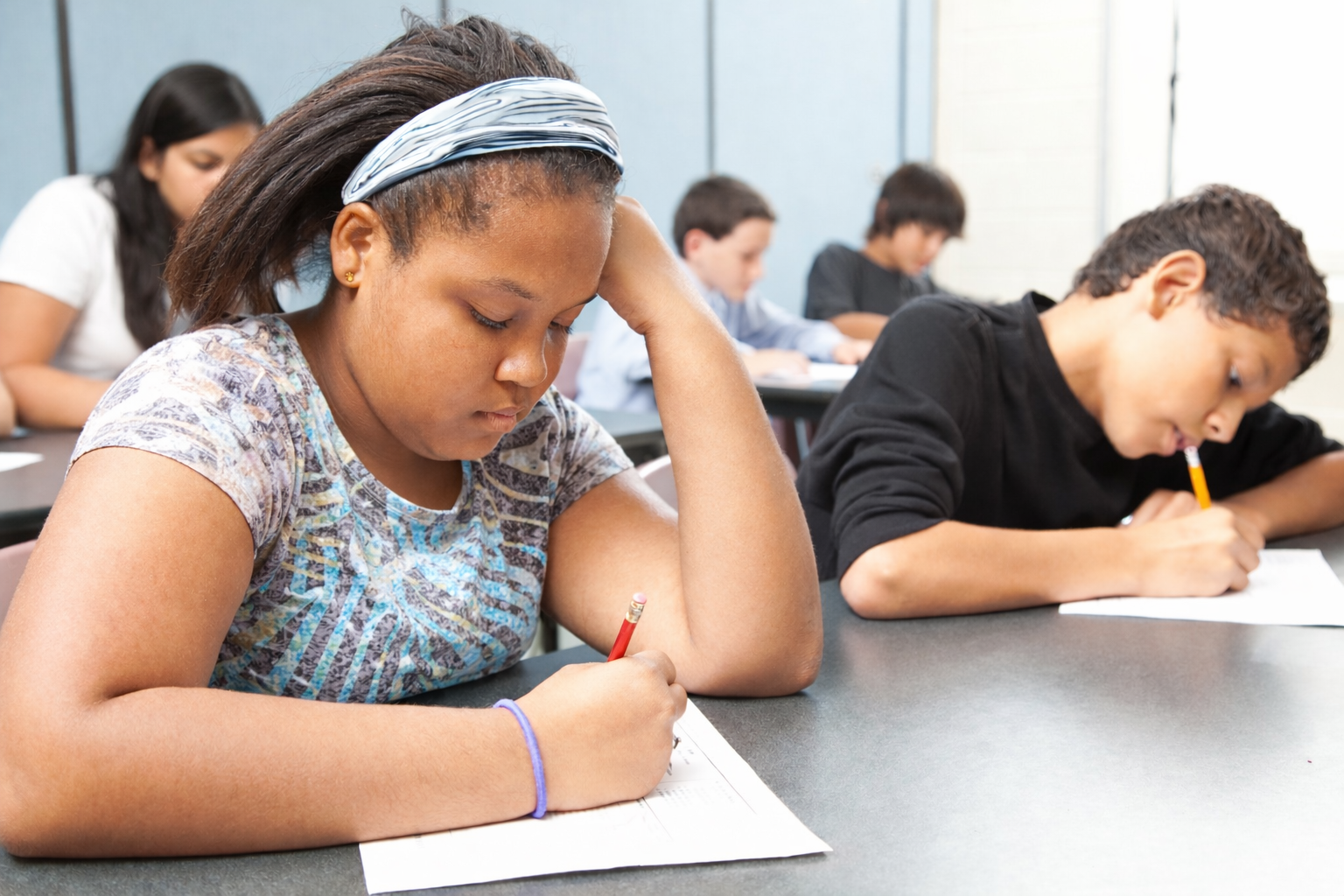 Middle school ELs writing at desks during a classroom assessment