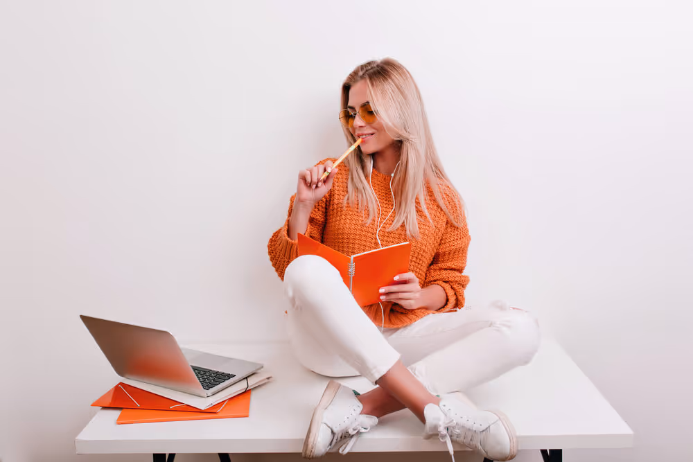 Woman sits on desk with laptop, in deep thought