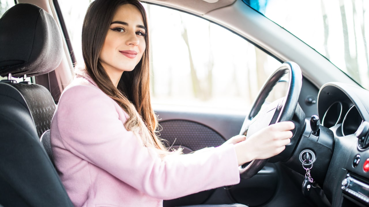 smiling female uber driver sitting in driver's seat of her car, hands on steering wheel