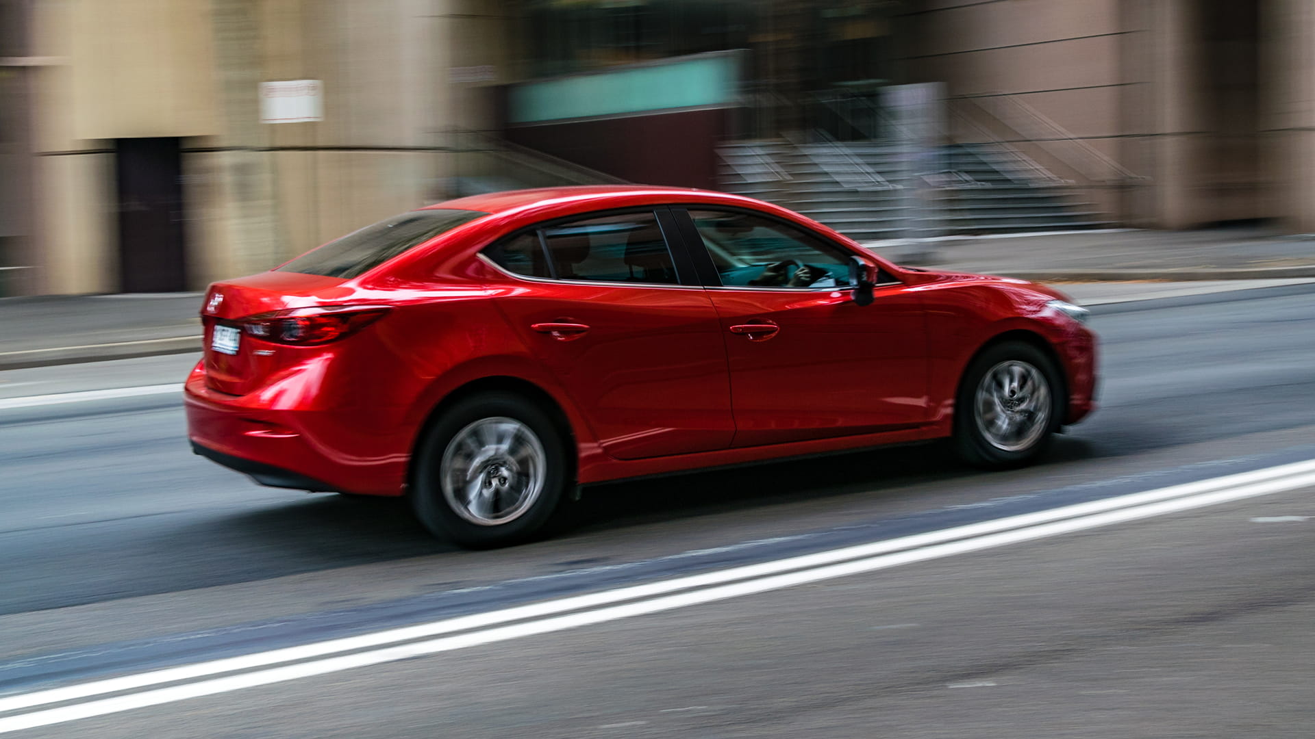 red sedan driving through a city representing employee business travel and vehicle reimbursement