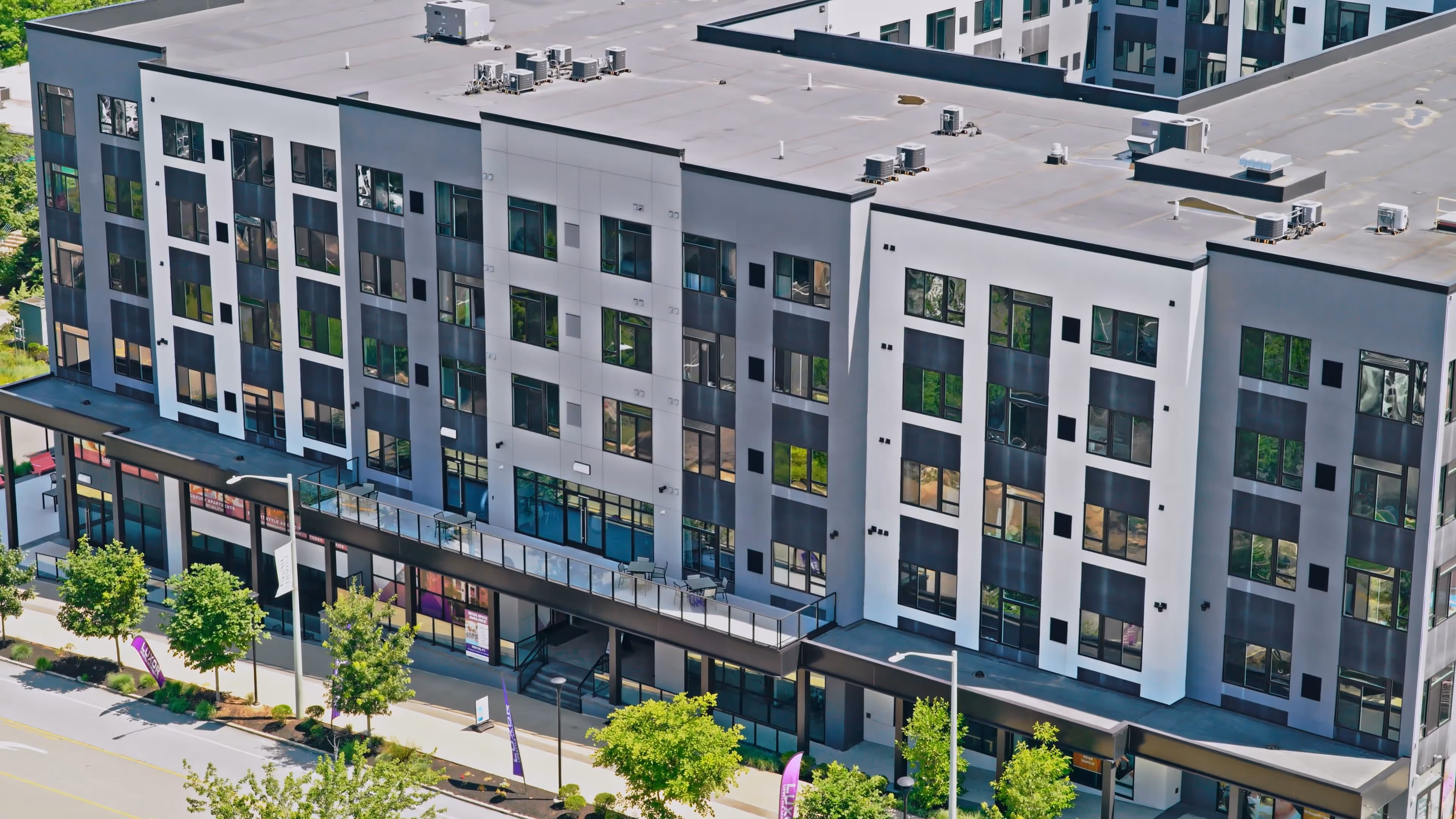Modern mid-rise apartment building with large windows, ground-floor retail space, and a streetscape lined with trees.