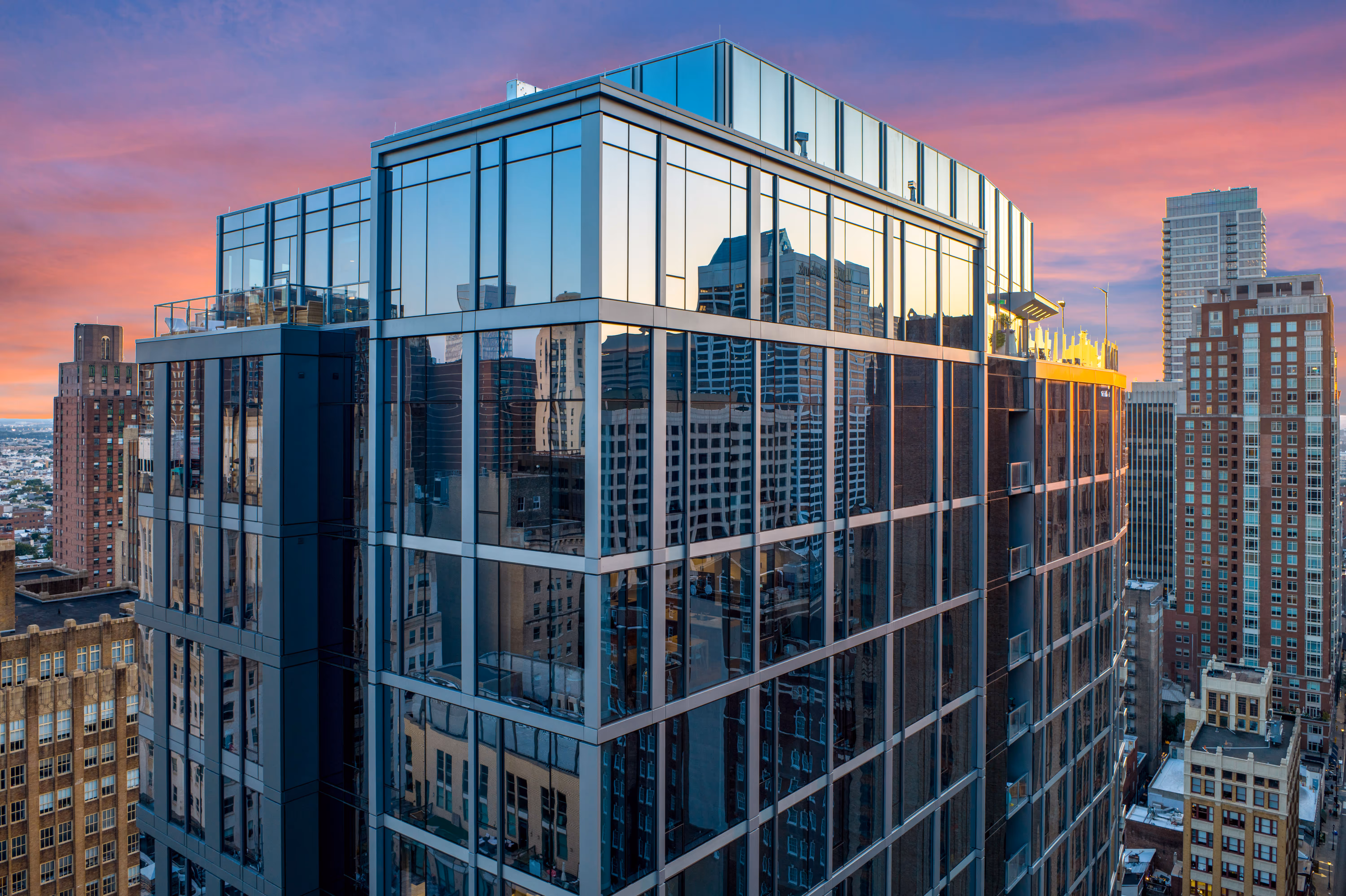 Glass high-rise building reflecting neighboring skyscrapers during a colorful sunset sky.