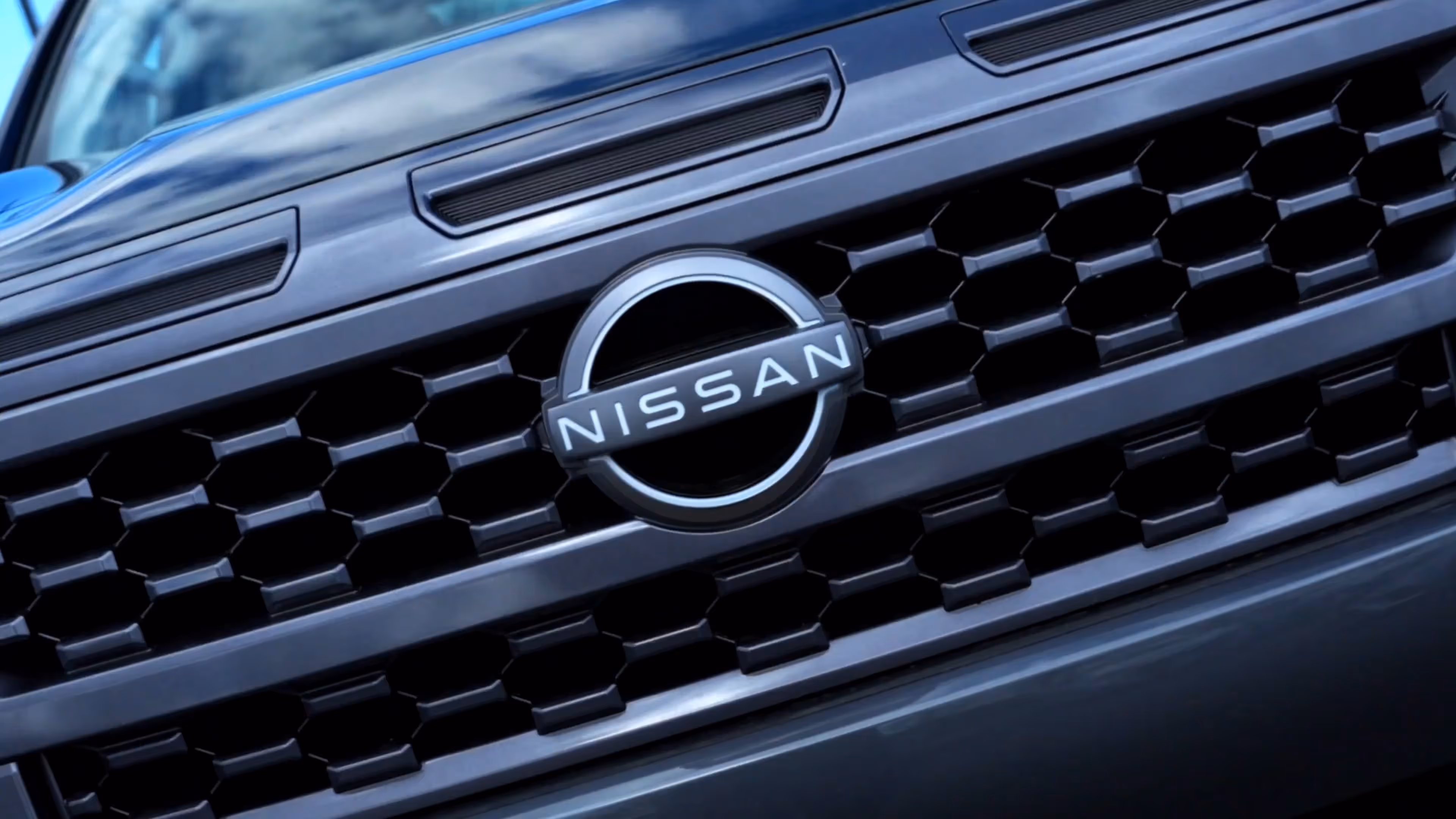 Close-up of a black Nissan car grille with the Nissan emblem in the center.