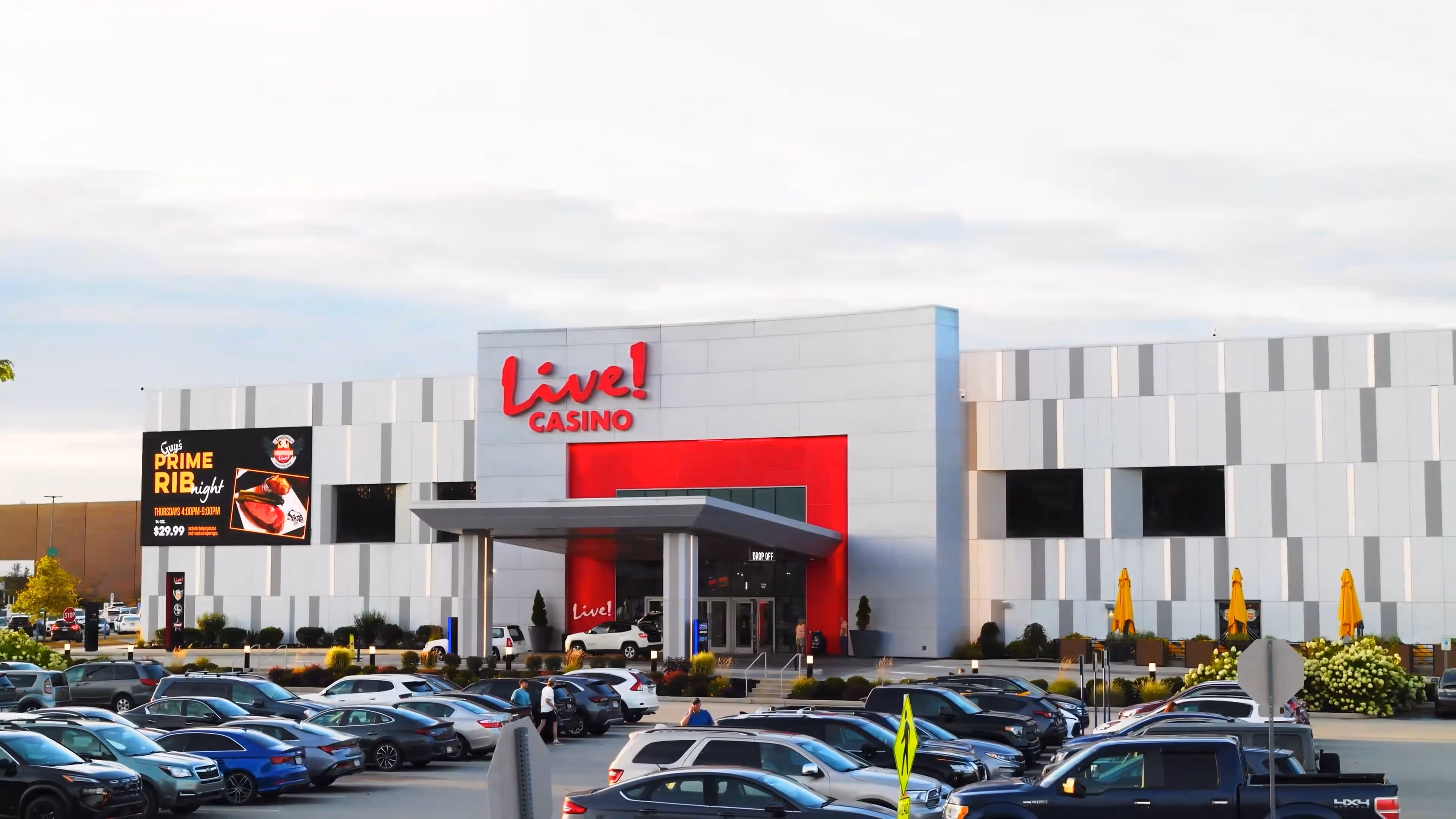 Exterior view of Live! Casino building with a parking lot full of cars in front and a large sign advertising Prime Rib night.