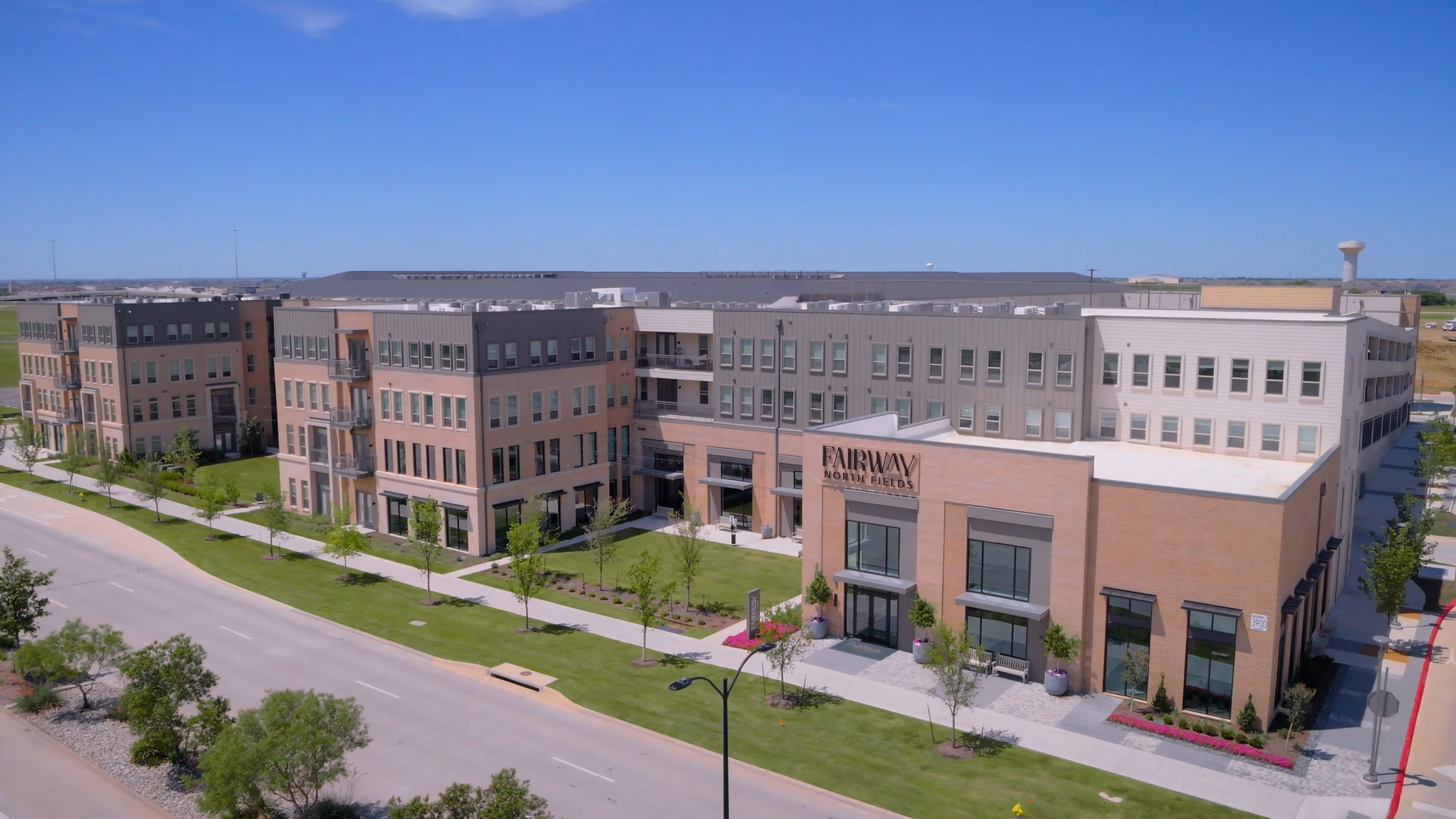 Large modern multi-family complex named Fairway North Fields with green lawns and clear sky.