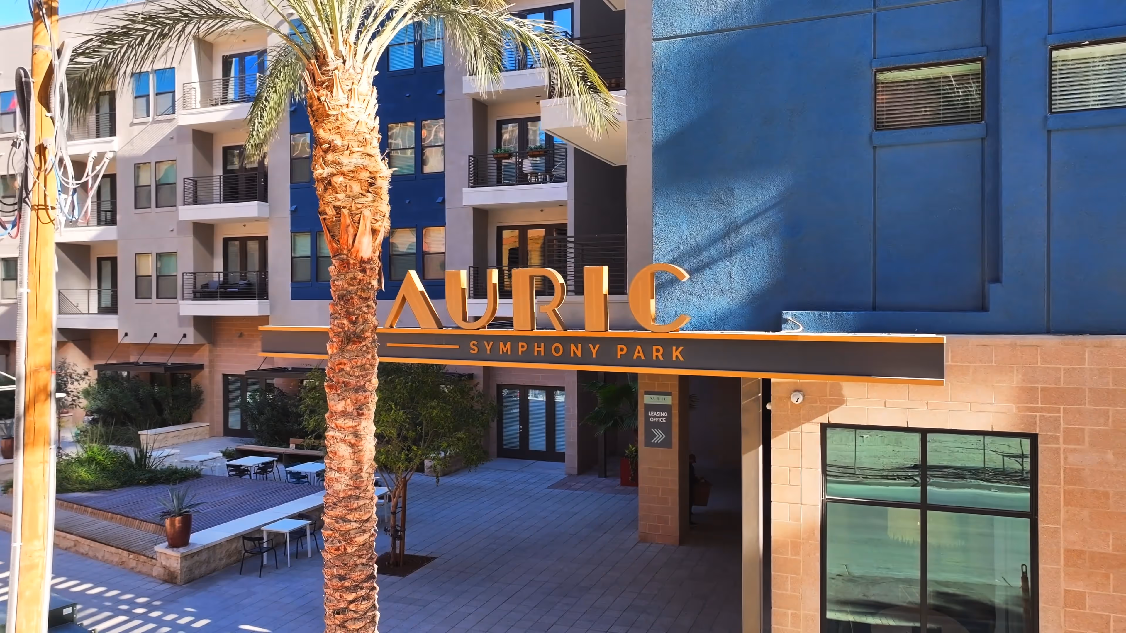 Exterior of Auric Symphony Park apartment building with palm tree and courtyard seating area.