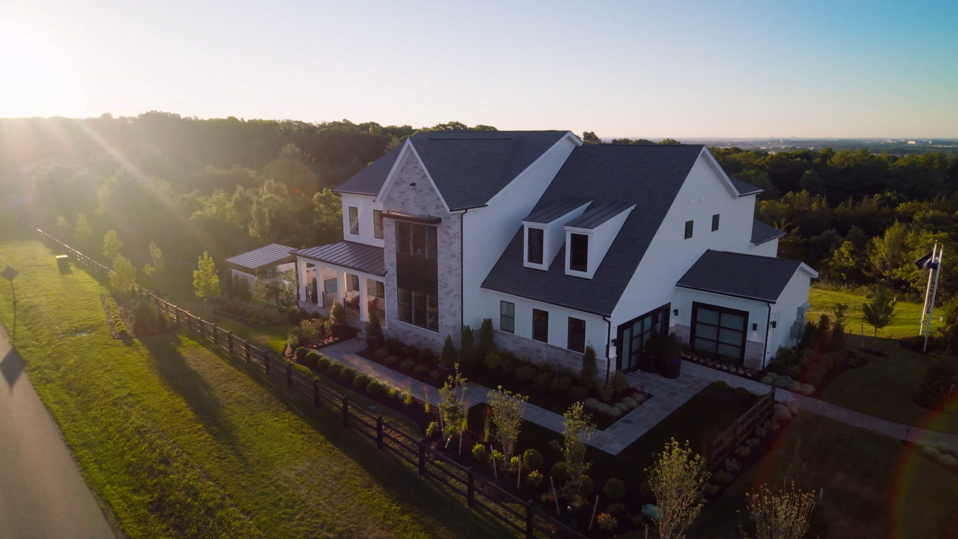 Large white two-story house with dark roof and landscaped yard at sunset.