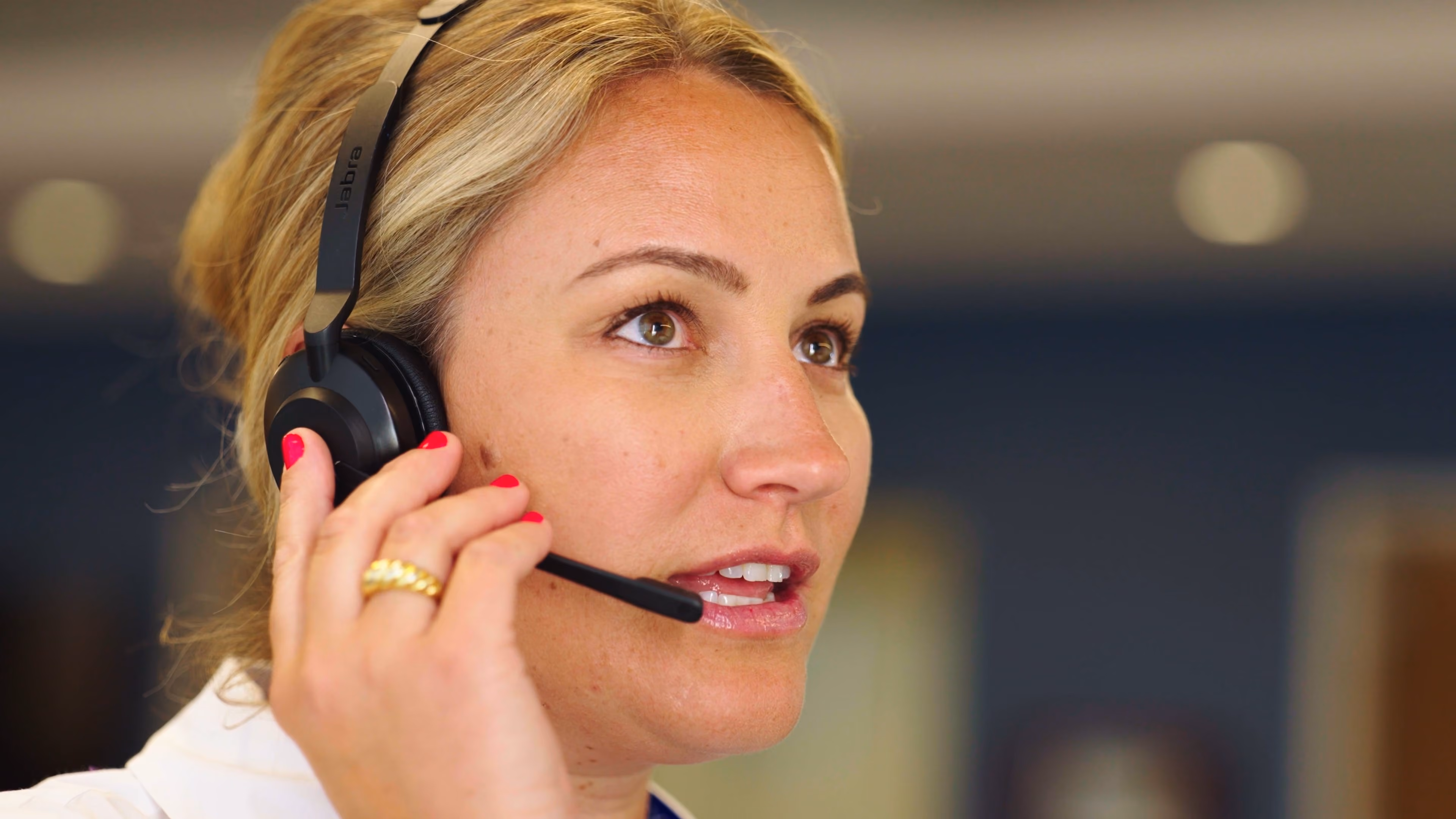 Close-up of a woman speaking while wearing a black Jabra headset and holding its microphone.