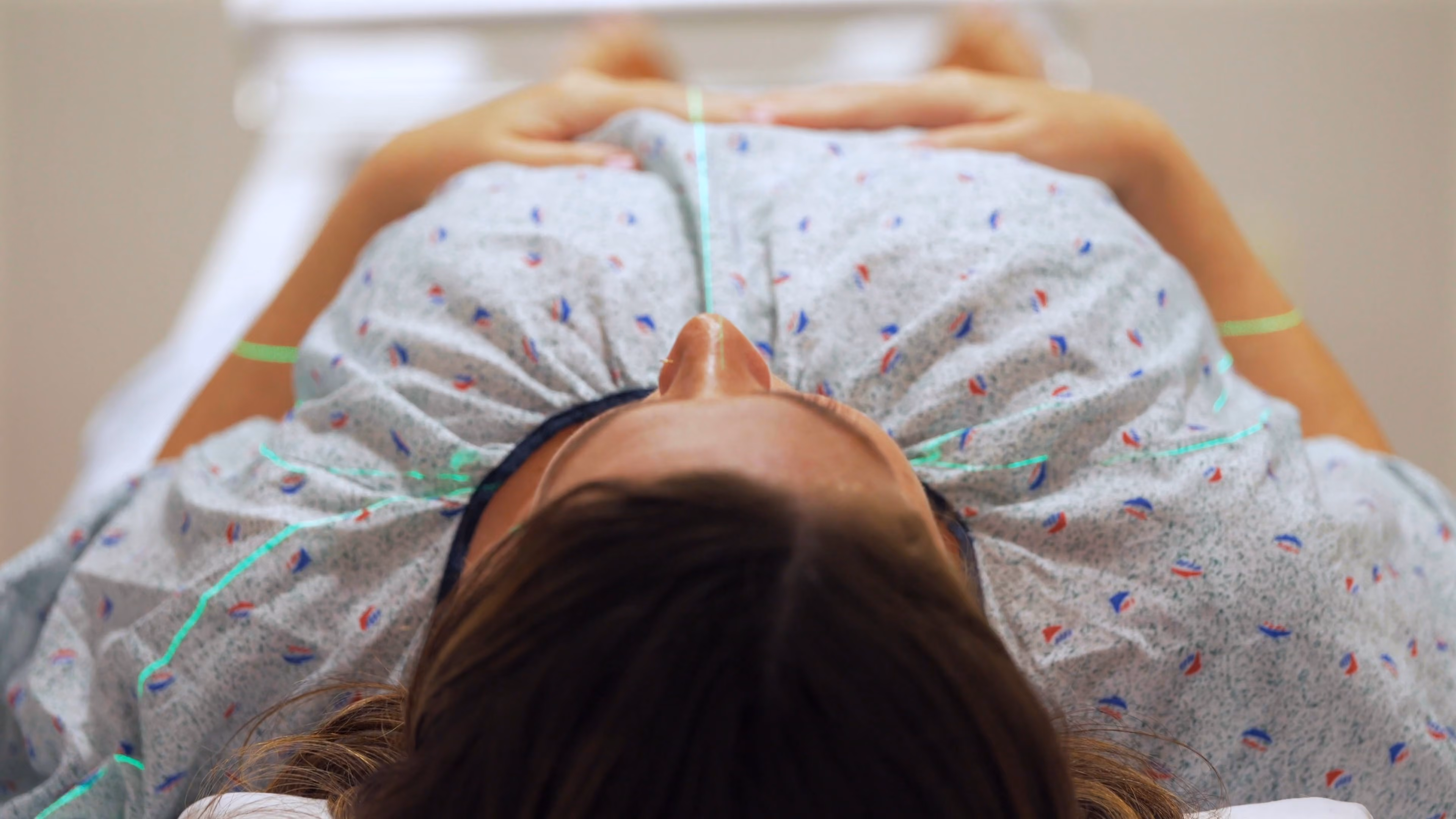 Overhead view of a woman in a medical gown lying down with green scanning lines on her chest.