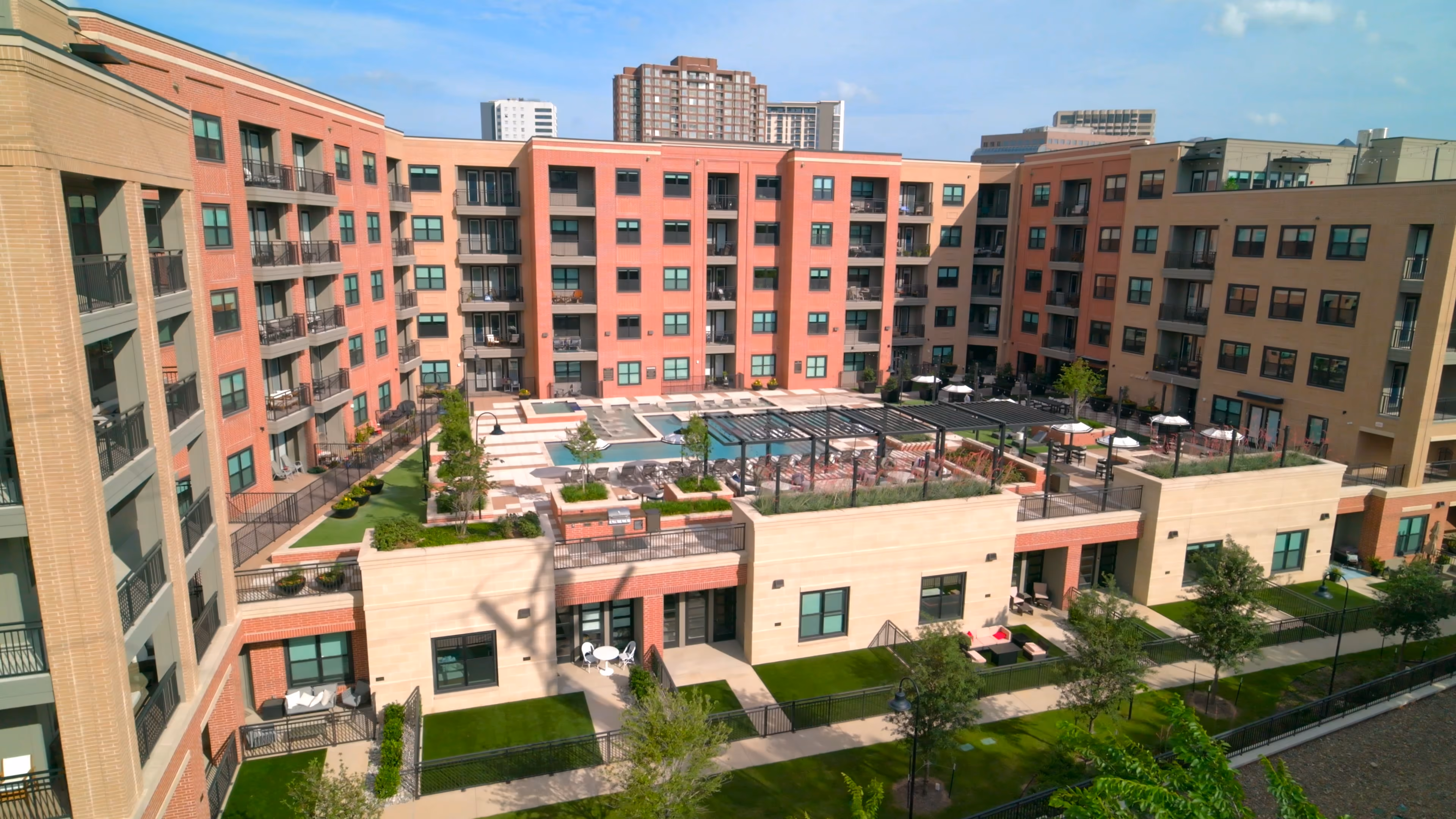 Modern apartment complex with central courtyard featuring a pool, lounge areas, and greenery.