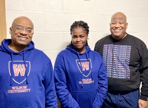 Three individuals standing together wearing college merch