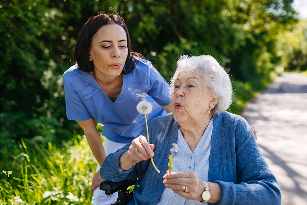 Female nurse blowing dandelion with elderly woman