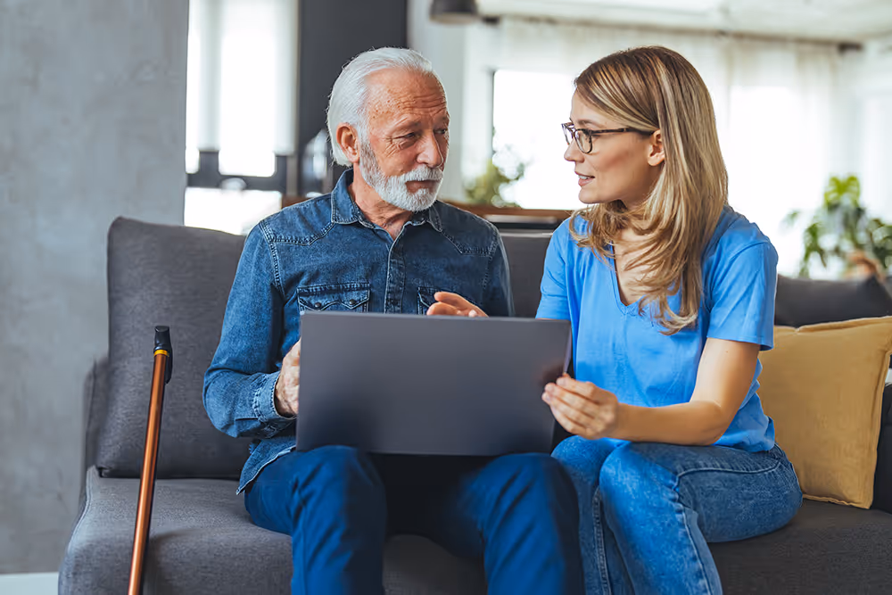 Woman sitting next to elderly man with laptop