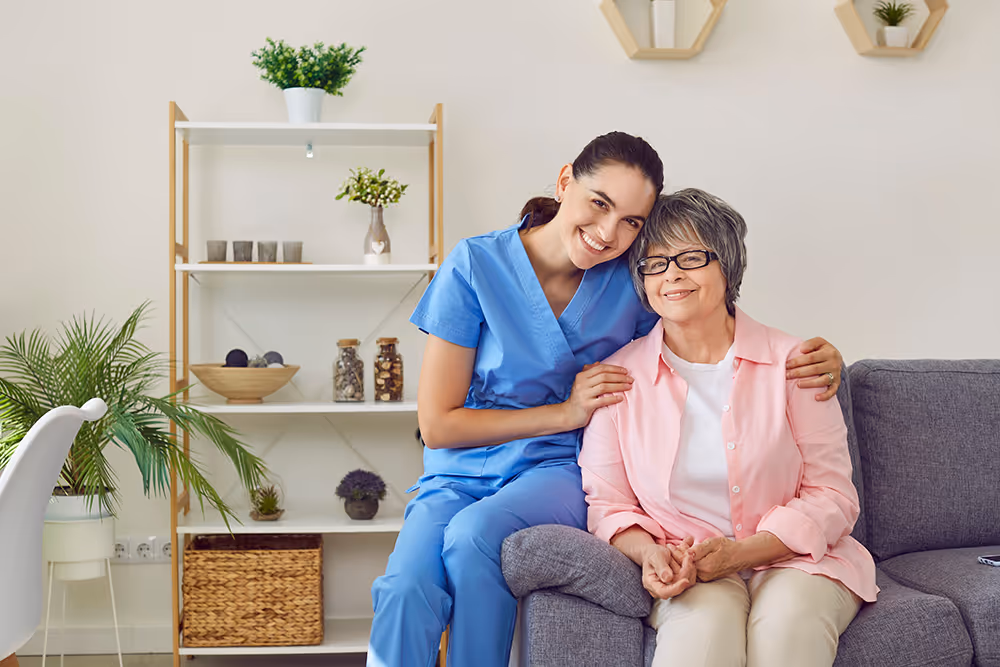 Young female nurse sitting and hugging with elderly woman on lounge