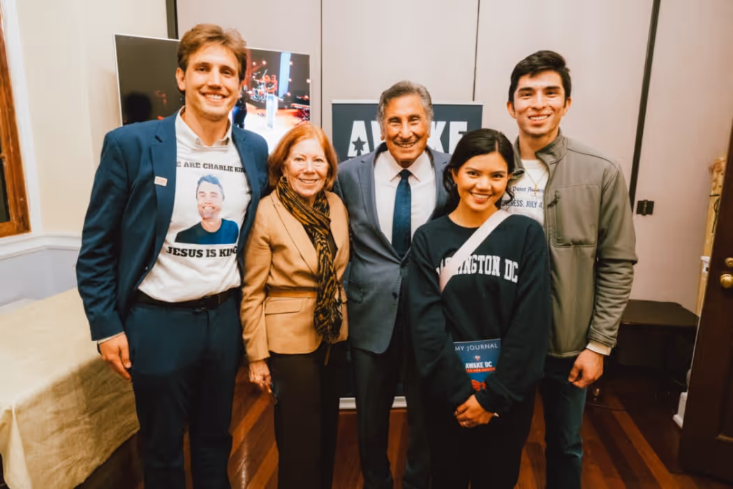 A group of attendees poses for a photo indoors, with Dr. Michael Youssef standing at the center, surrounded by smiling participants holding event materials.