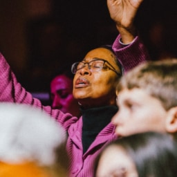 A woman lifting her hand in heartfelt prayer among the crowd, seeking God and believing for awakening.