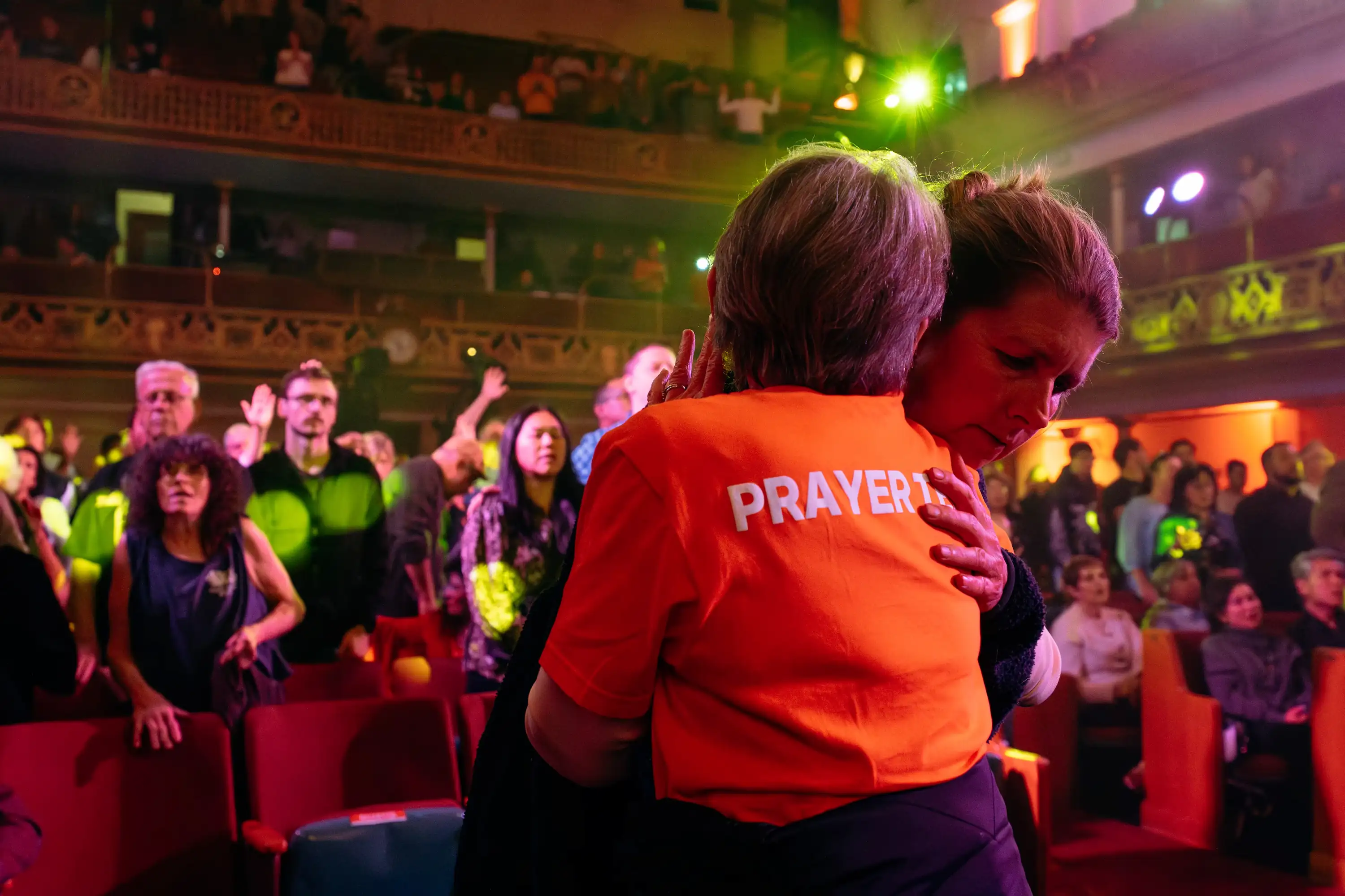Prayer minister embracing an attendee at AWAKE America Boston rally, crowd with raised hands in background