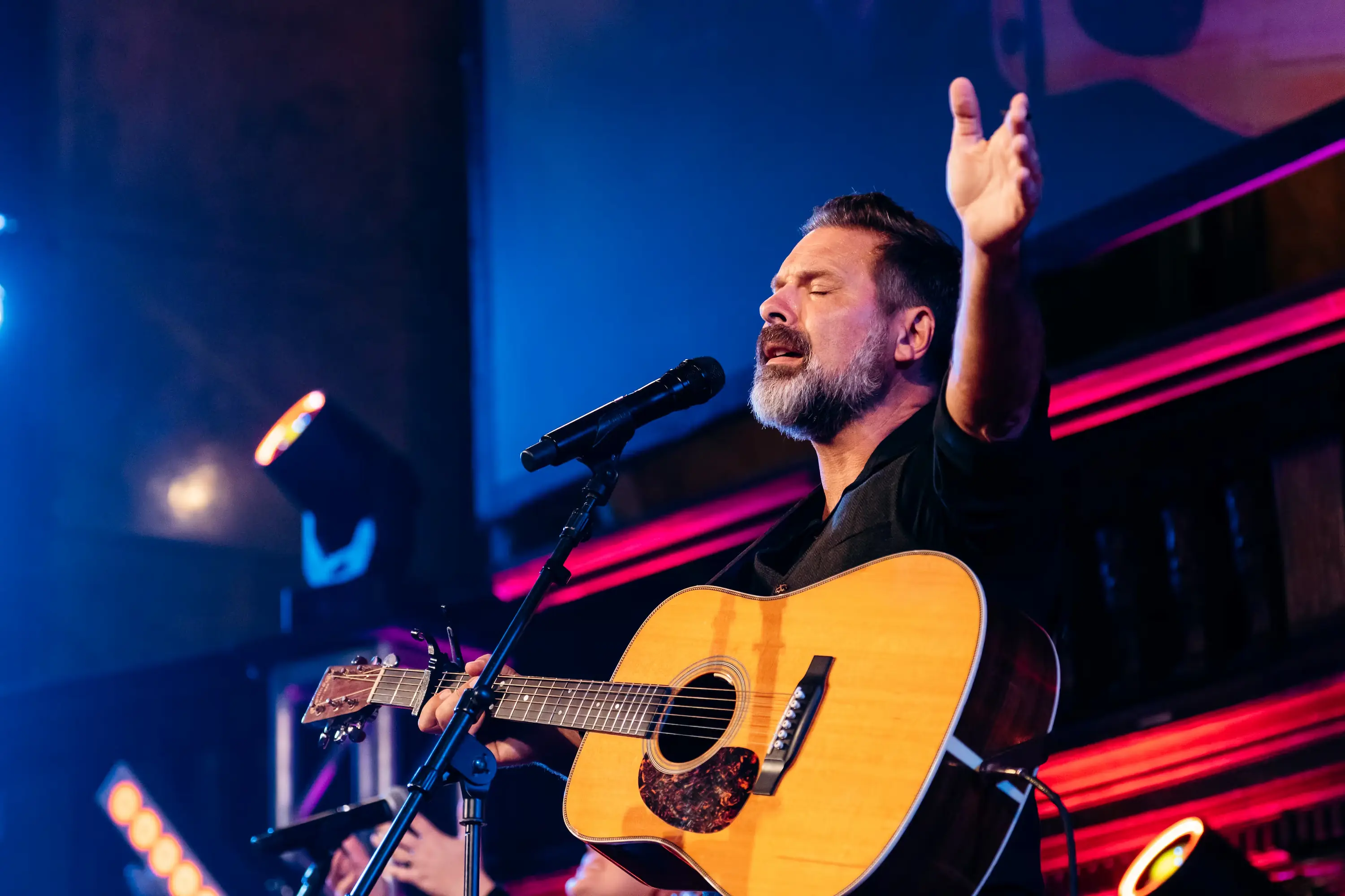 Worship leader playing acoustic guitar with hand raised at AWAKE America Boston rally