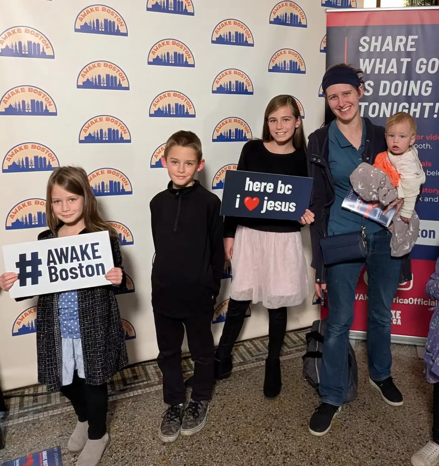 Family with children at AWAKE Boston photo booth holding revival and #AWAKE Boston signs