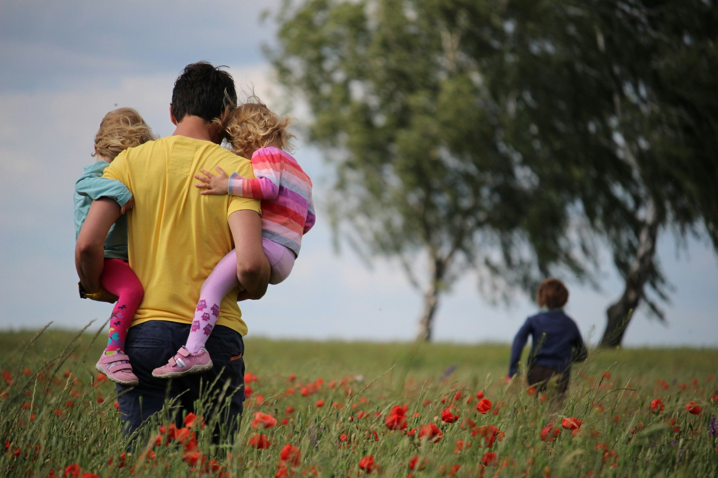 Father carrying two young children through a red poppy field while a third child walks ahead