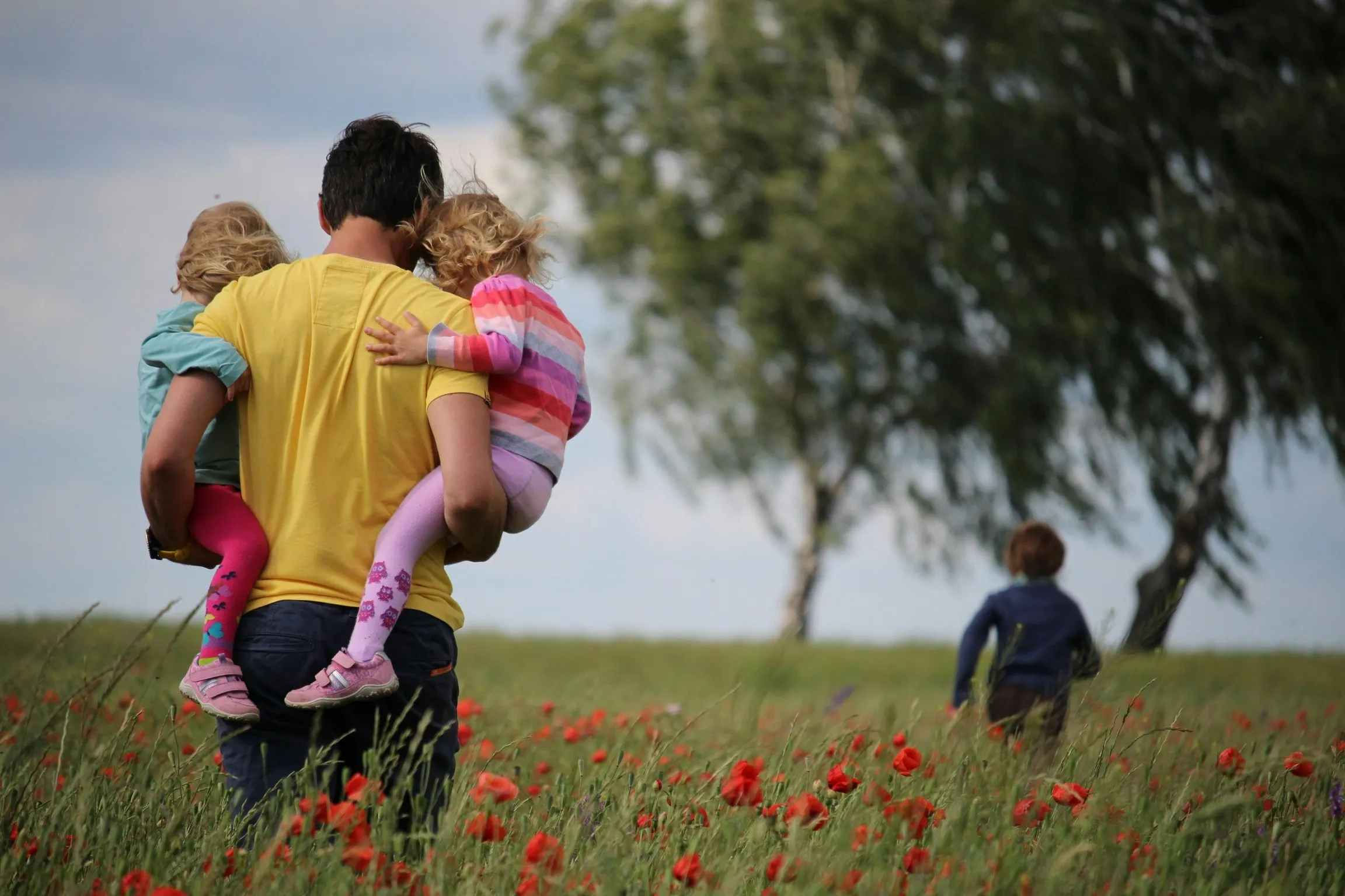 Father carrying two young children through a red poppy field while a third child walks ahead