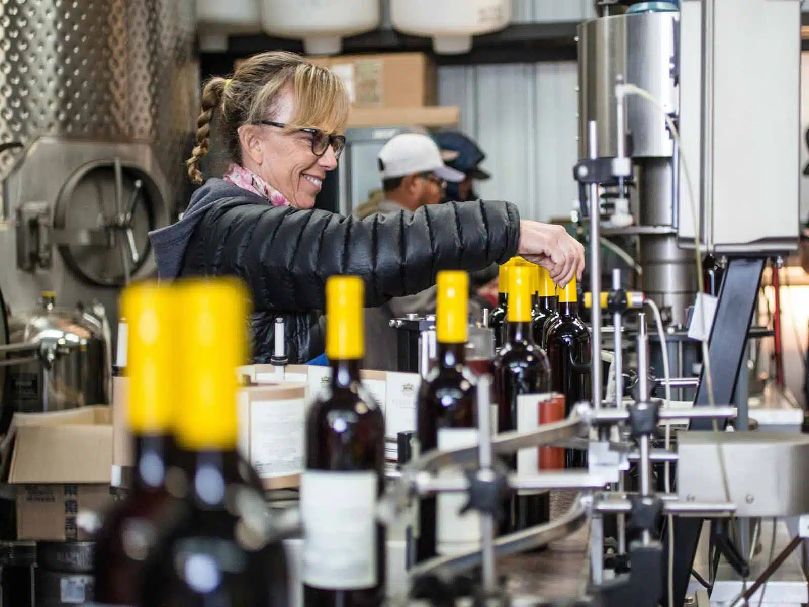 Woman smiling and placing yellow-capped bottles on an automated bottling line in a factory setting.