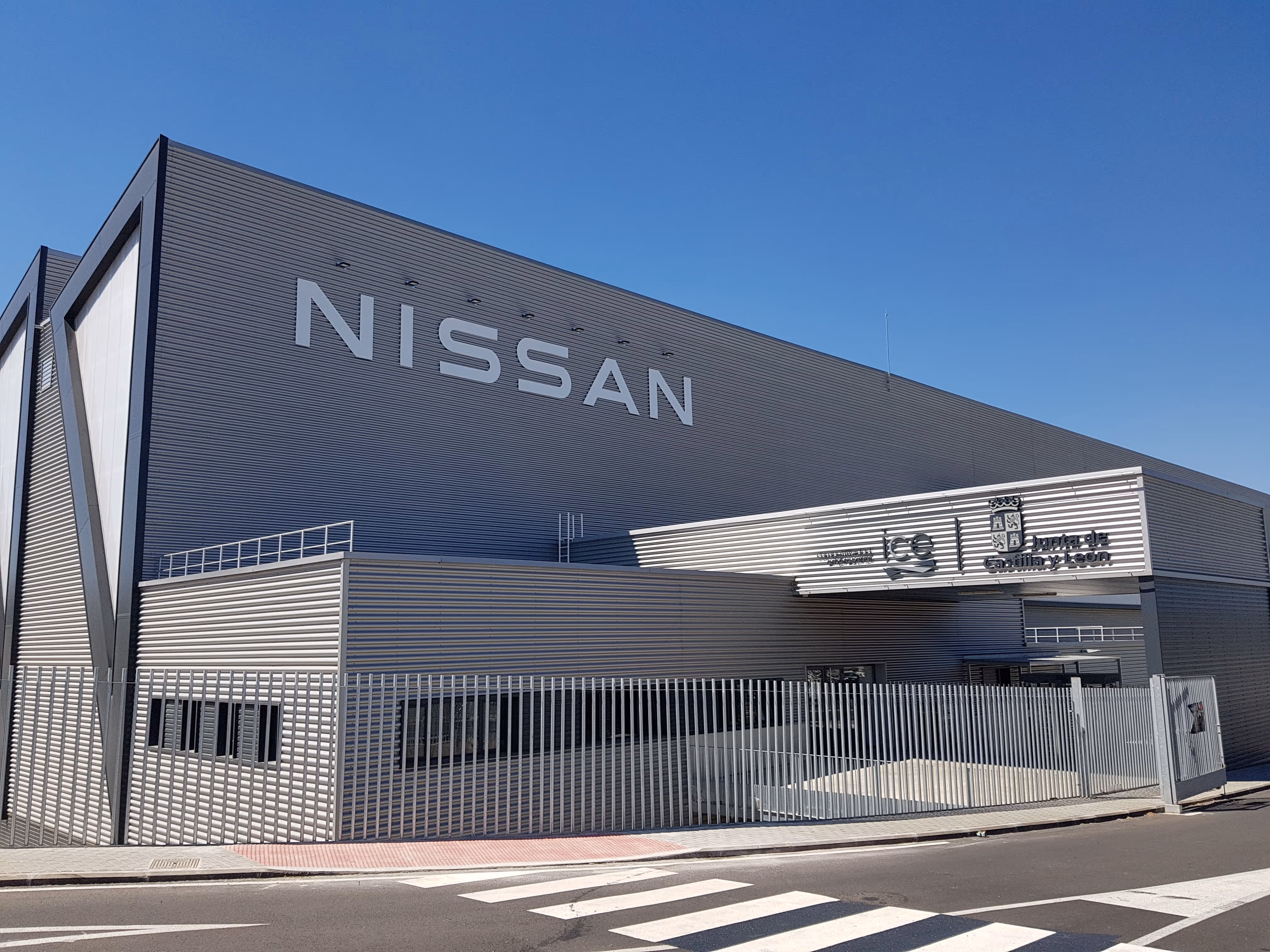 Exterior view of a modern Nissan manufacturing facility with gray metal siding under a clear blue sky.