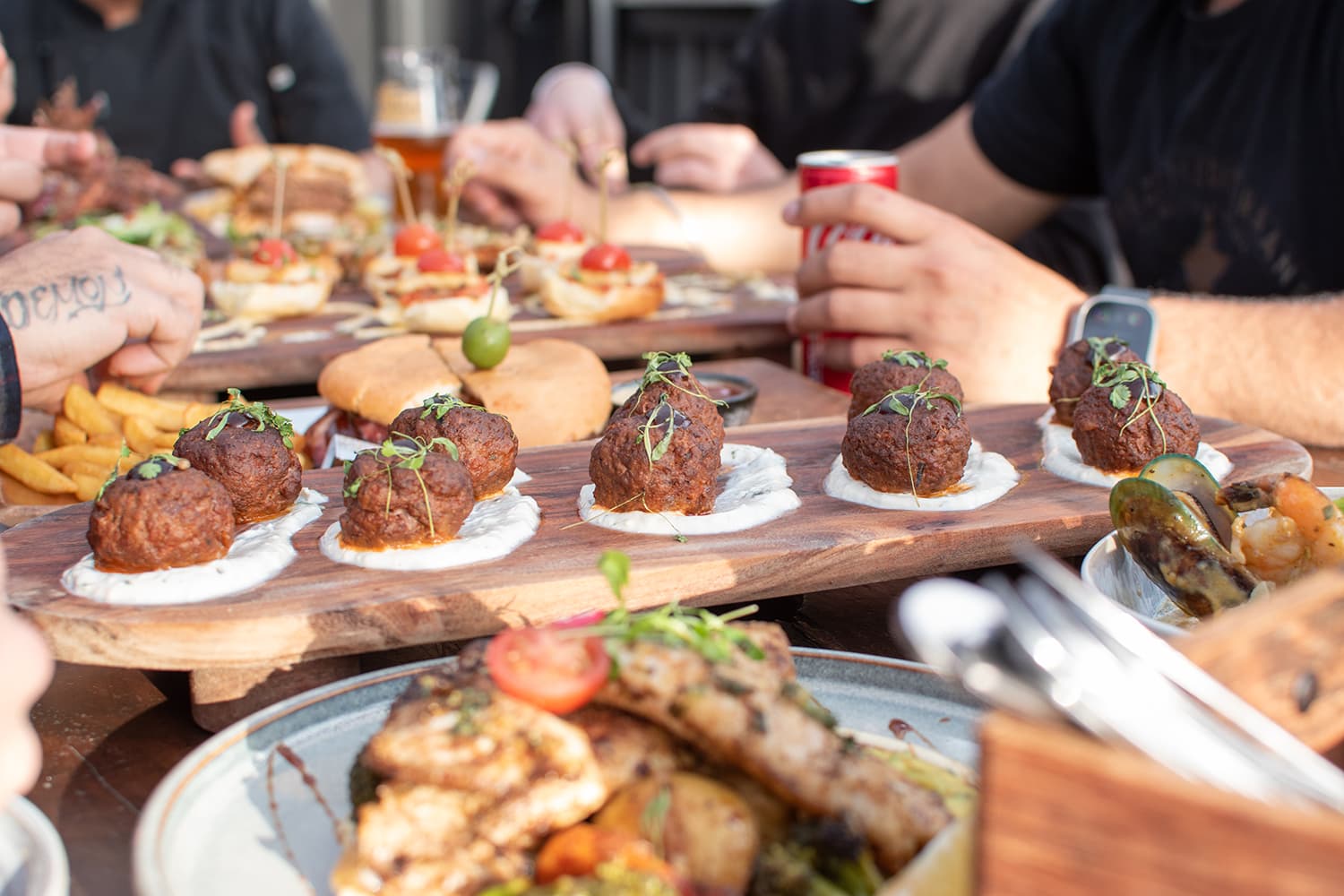 A wooden platter with meatballs, sliders, fries, and mussels served at a function at the Olive Kitchen and Bar