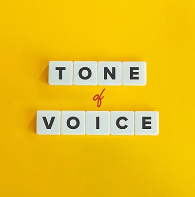 ellow background with white letter tiles spelling ‘Tone of Voice’ with ‘of’ in red script