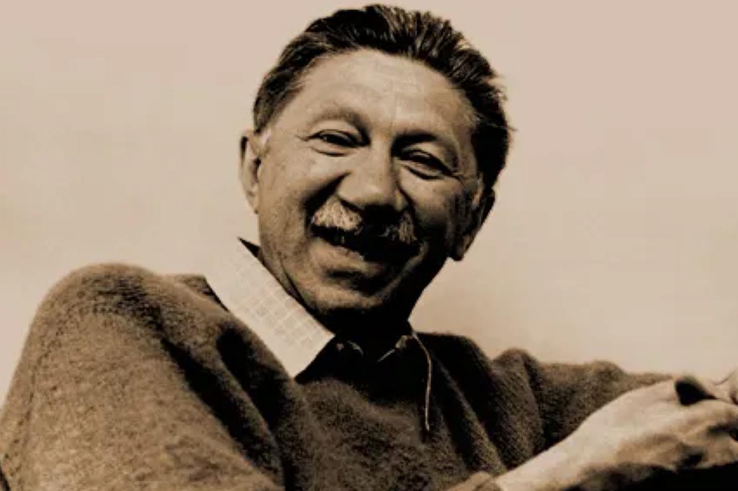 Sepia-toned portrait of a smiling man with a moustache wearing a sweater over a collared shirt, widely believed to be psychologist Abraham Maslow, known for creating Maslow’s hierarchy of needs