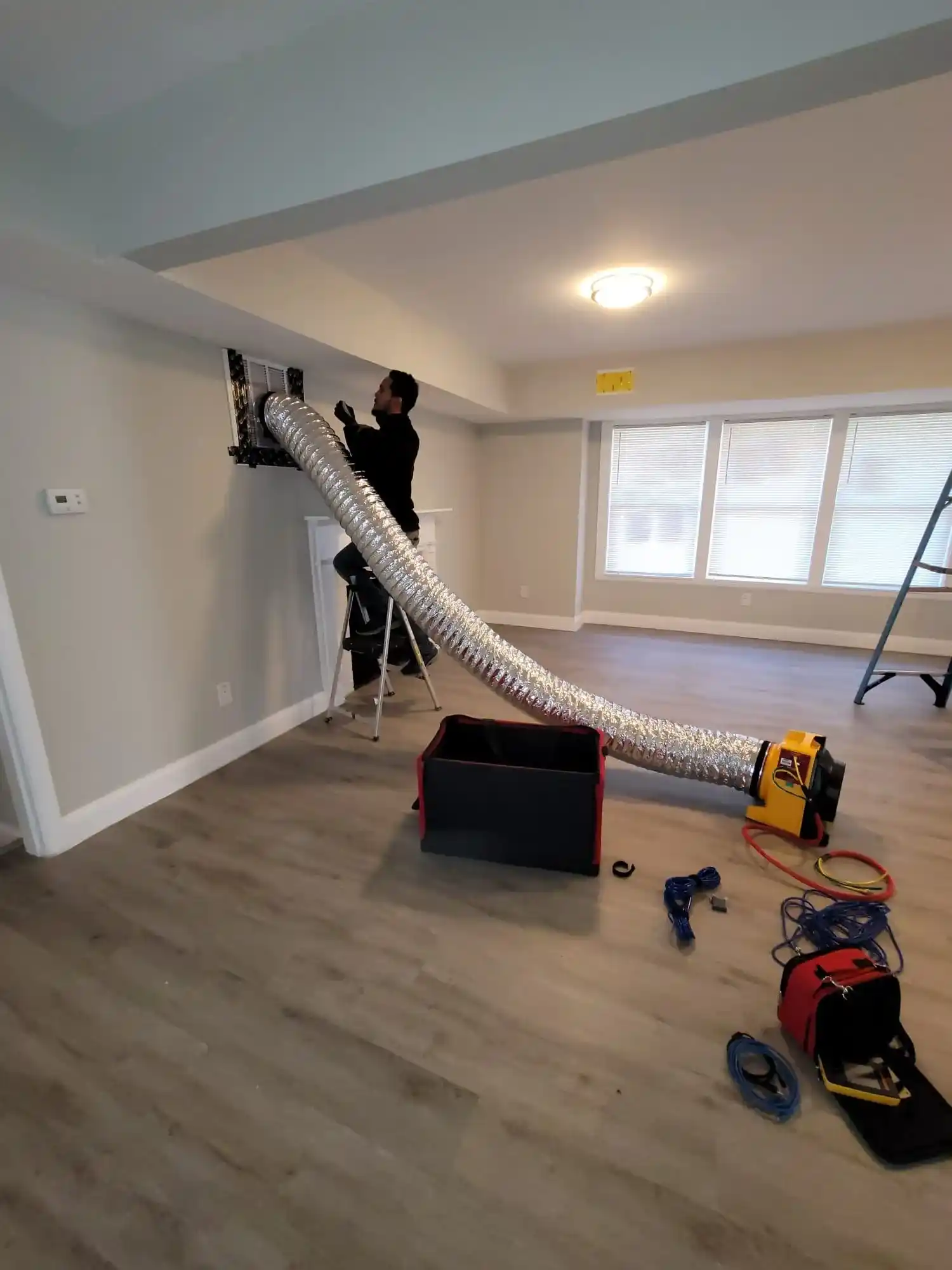 Worker installing large flexible duct in empty room with tools scattered around