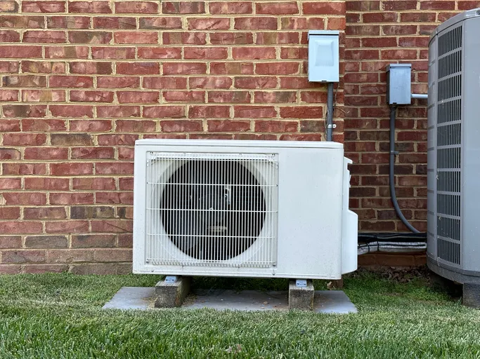 White air conditioning unit on concrete pad next to brick wall and grass