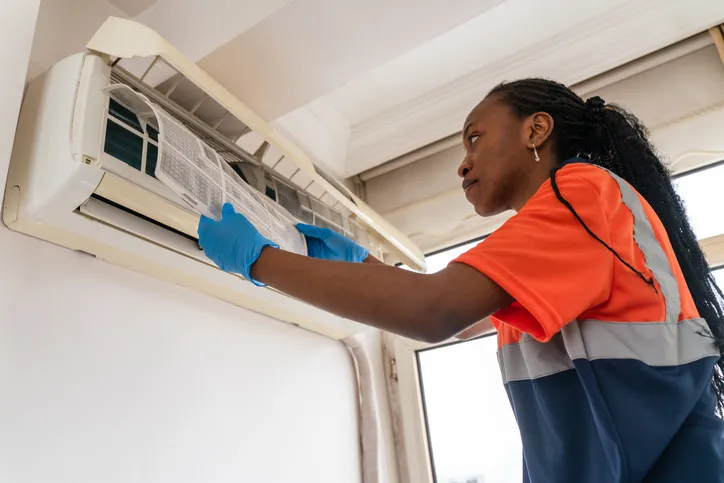 Technician in safety vest checking air conditioning unit with blue gloves