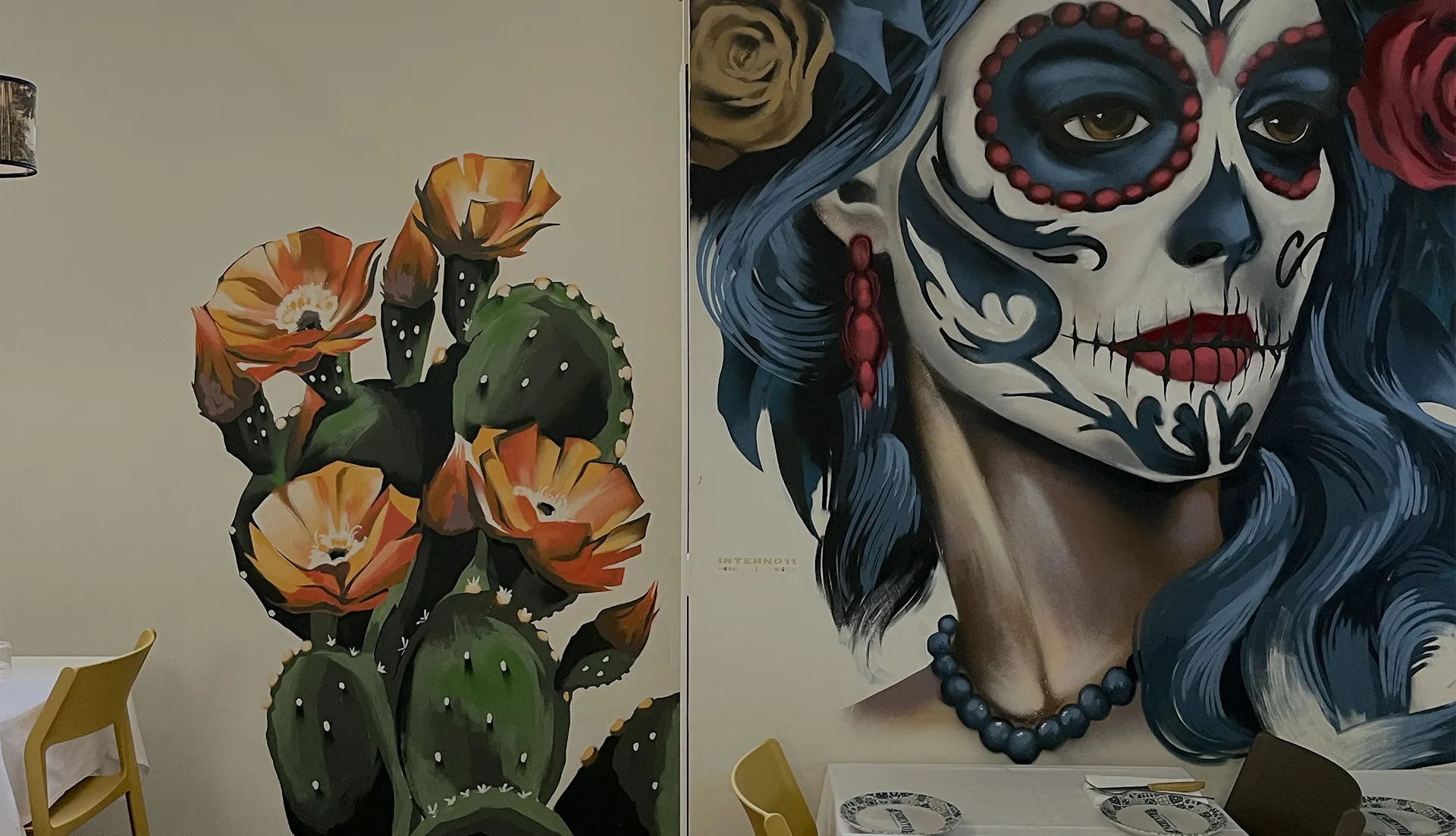 Murale dipinto a mano in stile messicano con volto Día de los Muertos e cactus in fiore sulle pareti di un locale