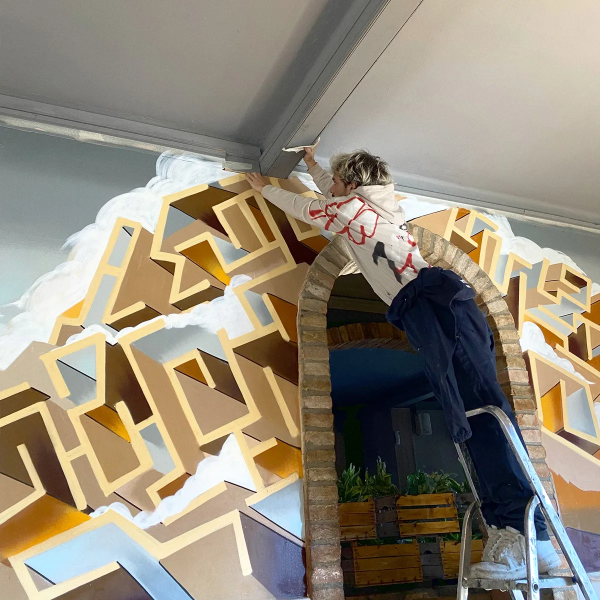 Artista di Interno Undici al lavoro su una scala mentre dipinge un'opera geometrica attorno a un arco in mattoni