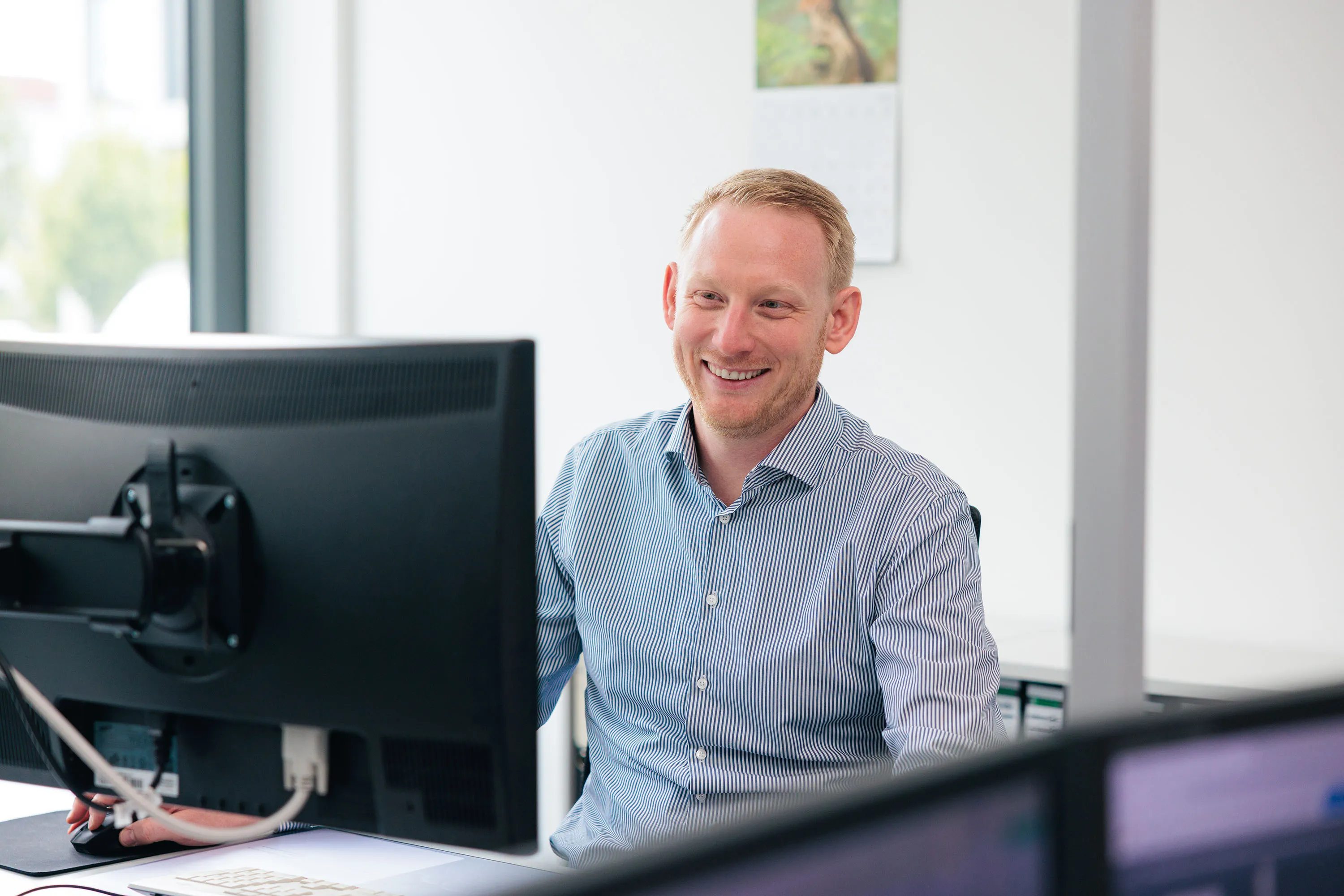 Mann sitzt am Schreibtisch und arbeitet an einem Computer in hellem Büro.